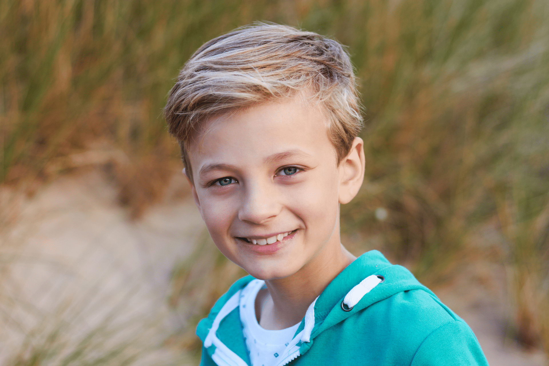 Smiling young boy outdoors wearing a teal hoodie